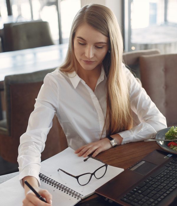 young-woman-writing-in-notebook-while-working-on-laptop-3874629